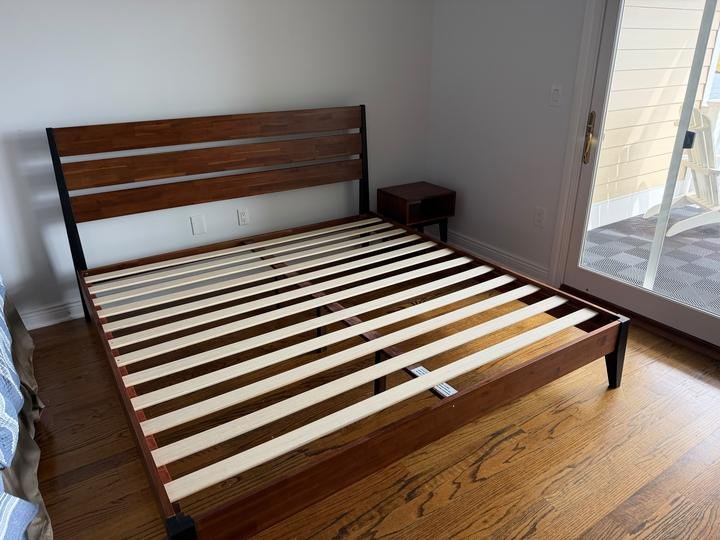 A wood platform bed frame with slats, assembled in a bedroom